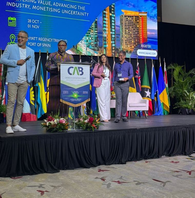 Gans Subramanian of B-TRNSFRMD on stage at the CAB 2025 Annual General Meeting and Conference, with the Caribbean Association of Banks podium and delegation flags.