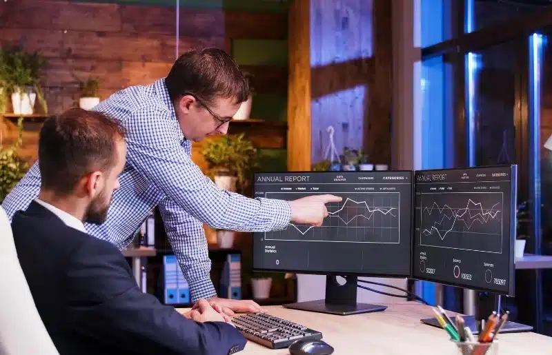 A team member pointing his hand on sales dashboard to other team member